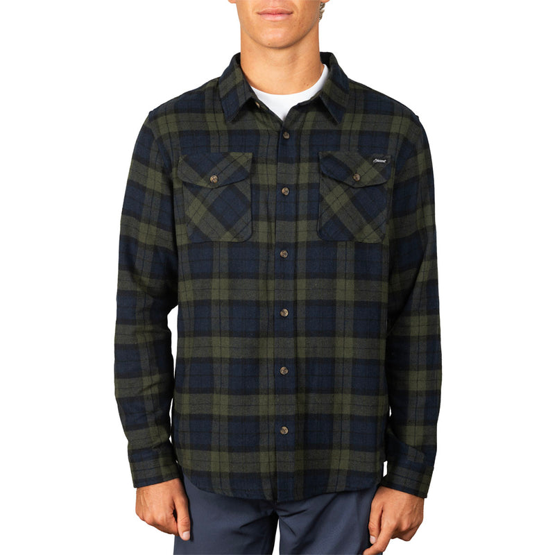A man wearing a long-sleeve plaid button-up shirt in dark navy and olive green, paired with dark blue pants, against a plain white background.