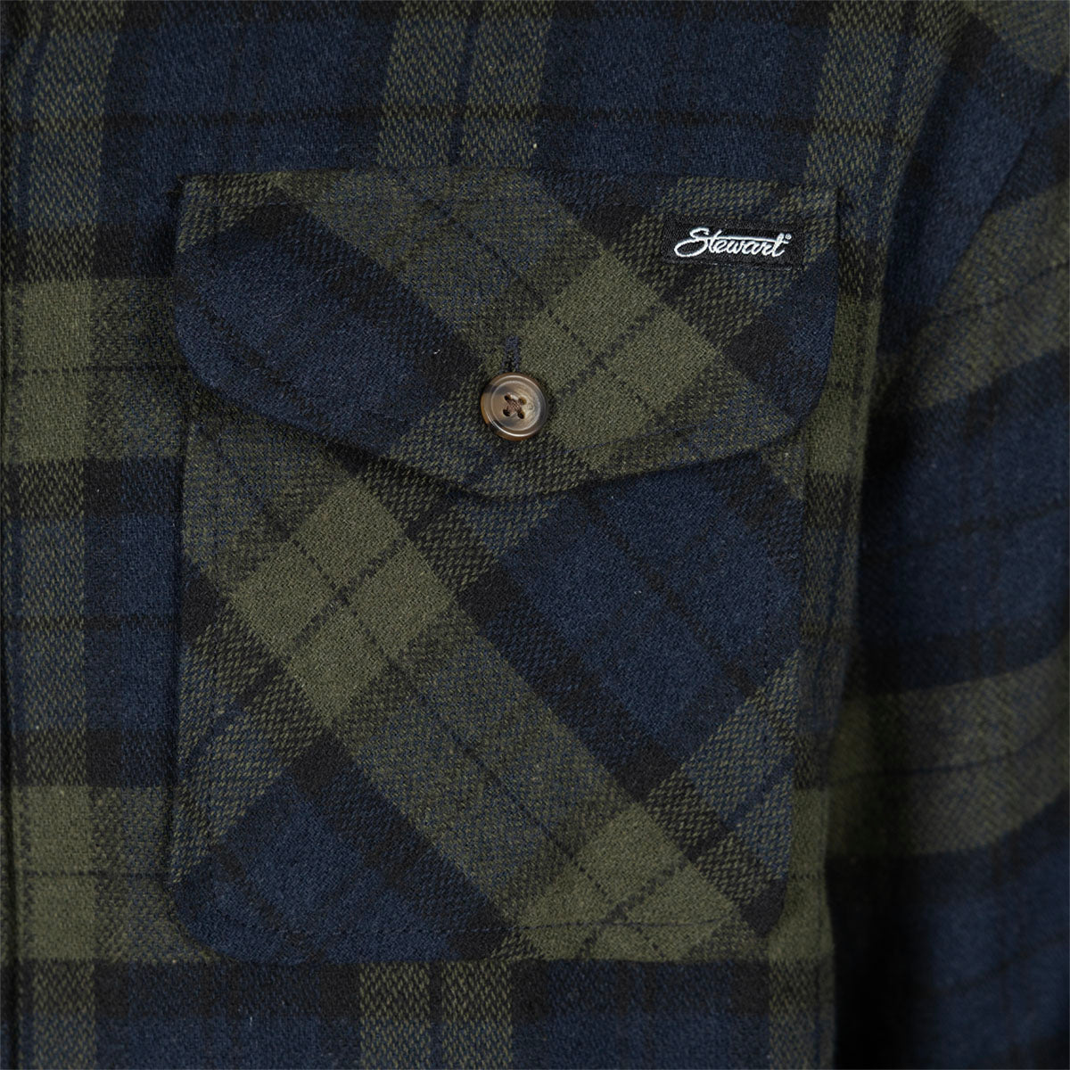 Close-up of a plaid flannel shirt pocket with a button flap. The fabric features a dark blue, olive green, and black tartan pattern, with a small white embroidered 'Street' logo on the chest pocket.