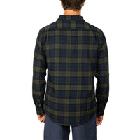A man viewed from the back wearing a long-sleeve plaid button-up shirt in dark navy and olive green, paired with navy pants, against a plain white background.