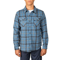 A man wearing a blue long-sleeve plaid button-up shirt with two chest pockets, paired with dark pants, against a plain white background.