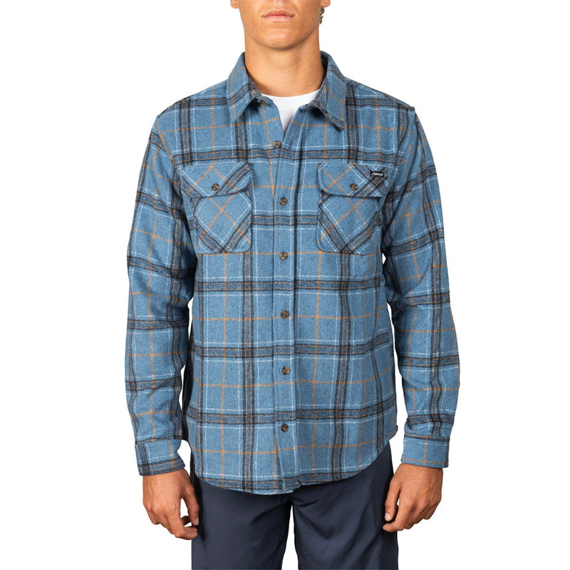 A man wearing a blue long-sleeve plaid button-up shirt with two chest pockets, paired with dark pants, against a plain white background.
