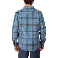 A man viewed from the back wearing a blue plaid flannel shirt with dark gray and orange lines, paired with navy pants, against a plain white background.
