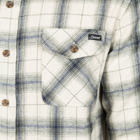 Close-up of a plaid button-up shirt with a chest pocket, featuring a white base with blue and gray plaid lines and a small black brand label on the pocket.