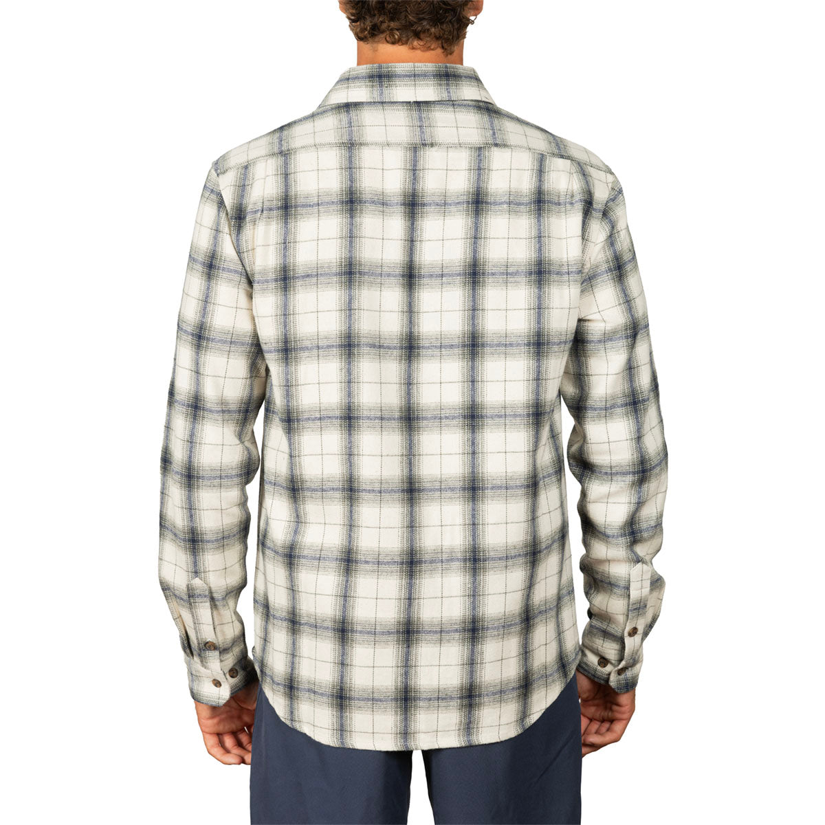A man viewed from the back wearing a long-sleeve plaid flannel shirt in cream and dark gray, paired with navy pants, against a plain white background.