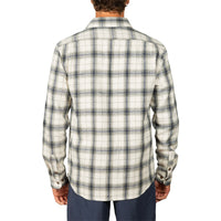A man viewed from the back wearing a long-sleeve plaid flannel shirt in cream and dark gray, paired with navy pants, against a plain white background.