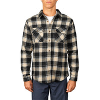A man wearing a long-sleeve button-up plaid flannel shirt in black and beige, paired with navy pants, against a plain white background.
