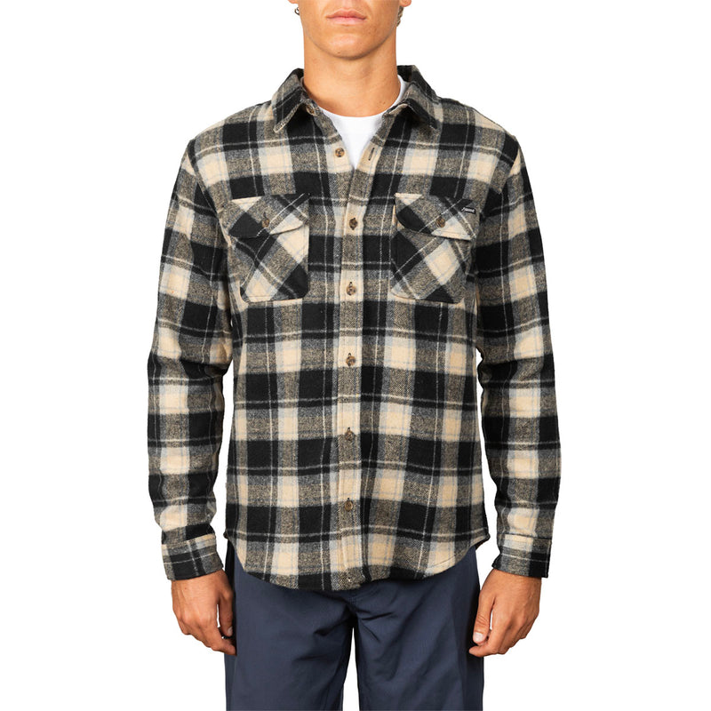 A man wearing a long-sleeve button-up plaid flannel shirt in black and beige, paired with navy pants, against a plain white background.
