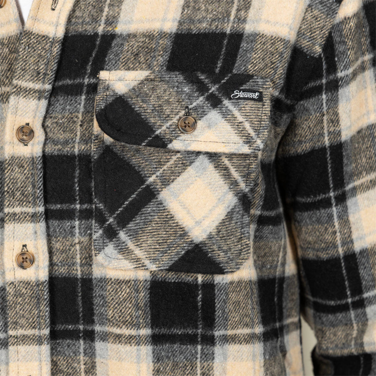 Close-up of a plaid flannel shirt with a chest pocket, featuring black, beige, and white check patterns and a small visible 'Savaget' brand tag.