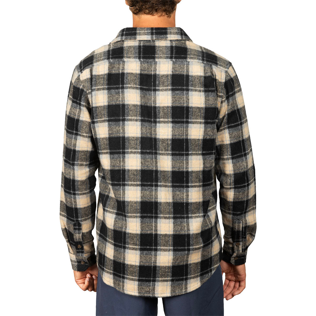 A man viewed from the back wearing a long-sleeve plaid flannel shirt in black and beige, paired with dark blue pants, against a plain white background.