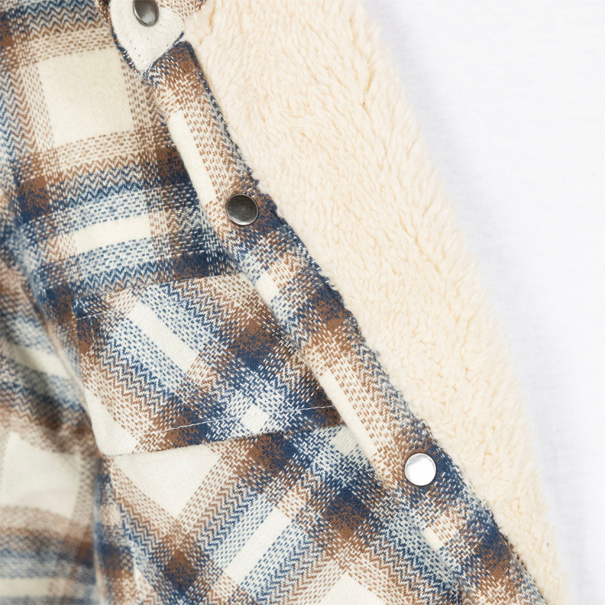 Close-up of a plaid flannel shirt with a cream sherpa lining and metal snap buttons.