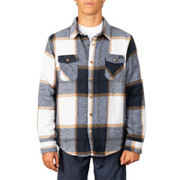 A man wearing a long-sleeve plaid button-up shirt in navy, gray, white, and tan, paired with dark pants, against a plain white background.