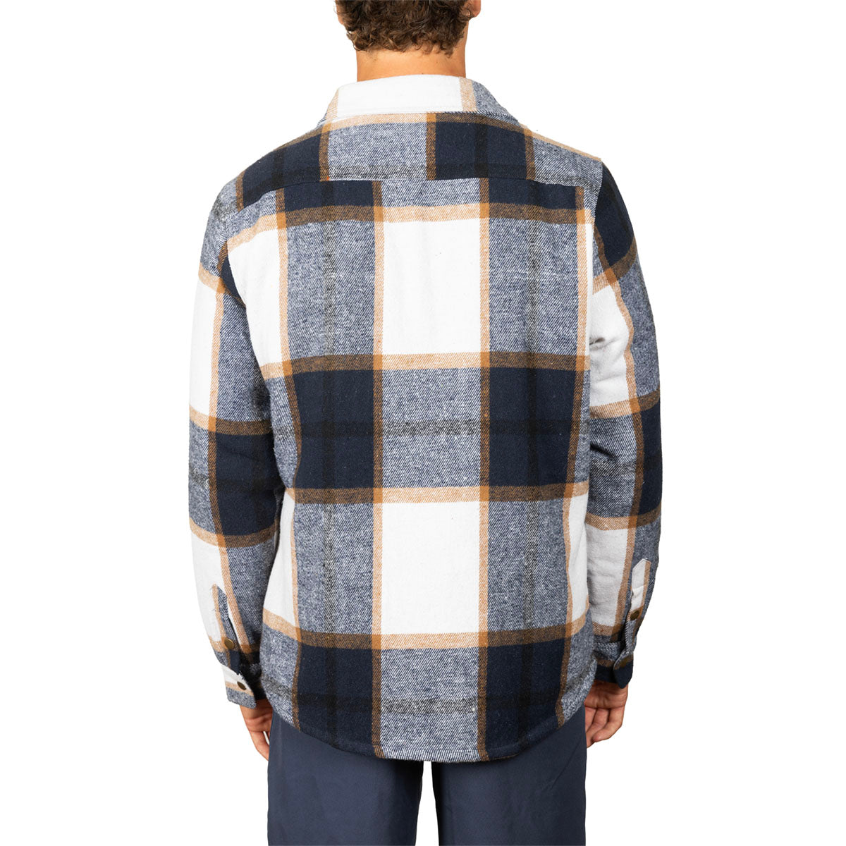 A man viewed from the back wearing a long-sleeve plaid flannel shirt in navy, gray, white, and tan, paired with dark blue pants, against a plain white background.