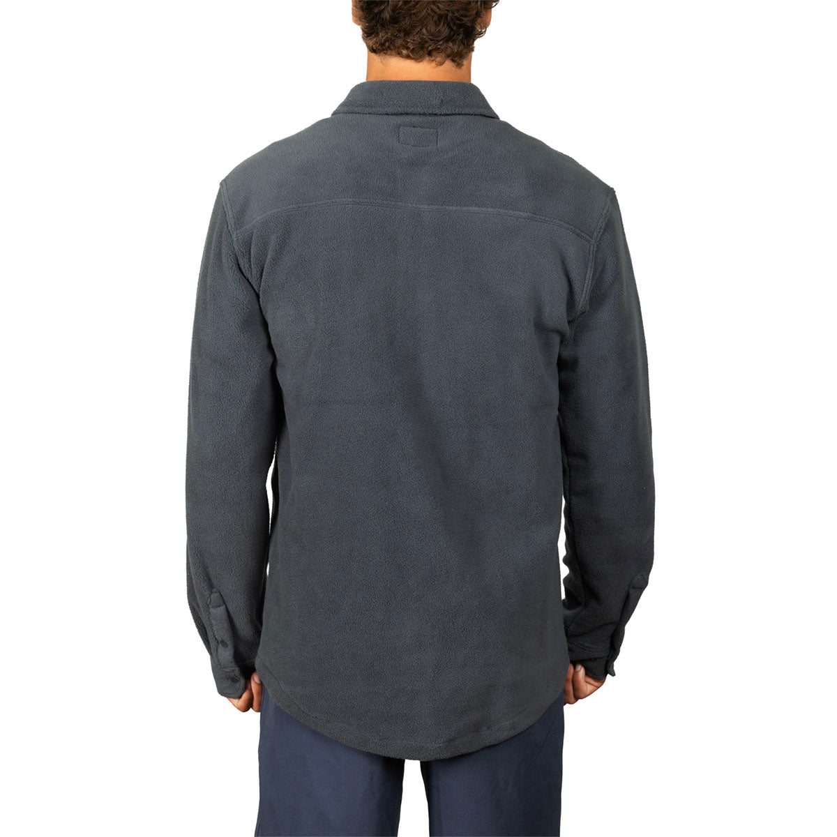 A man viewed from the back wearing a dark charcoal gray long-sleeve button-up shirt and navy pants, set against a plain white background.