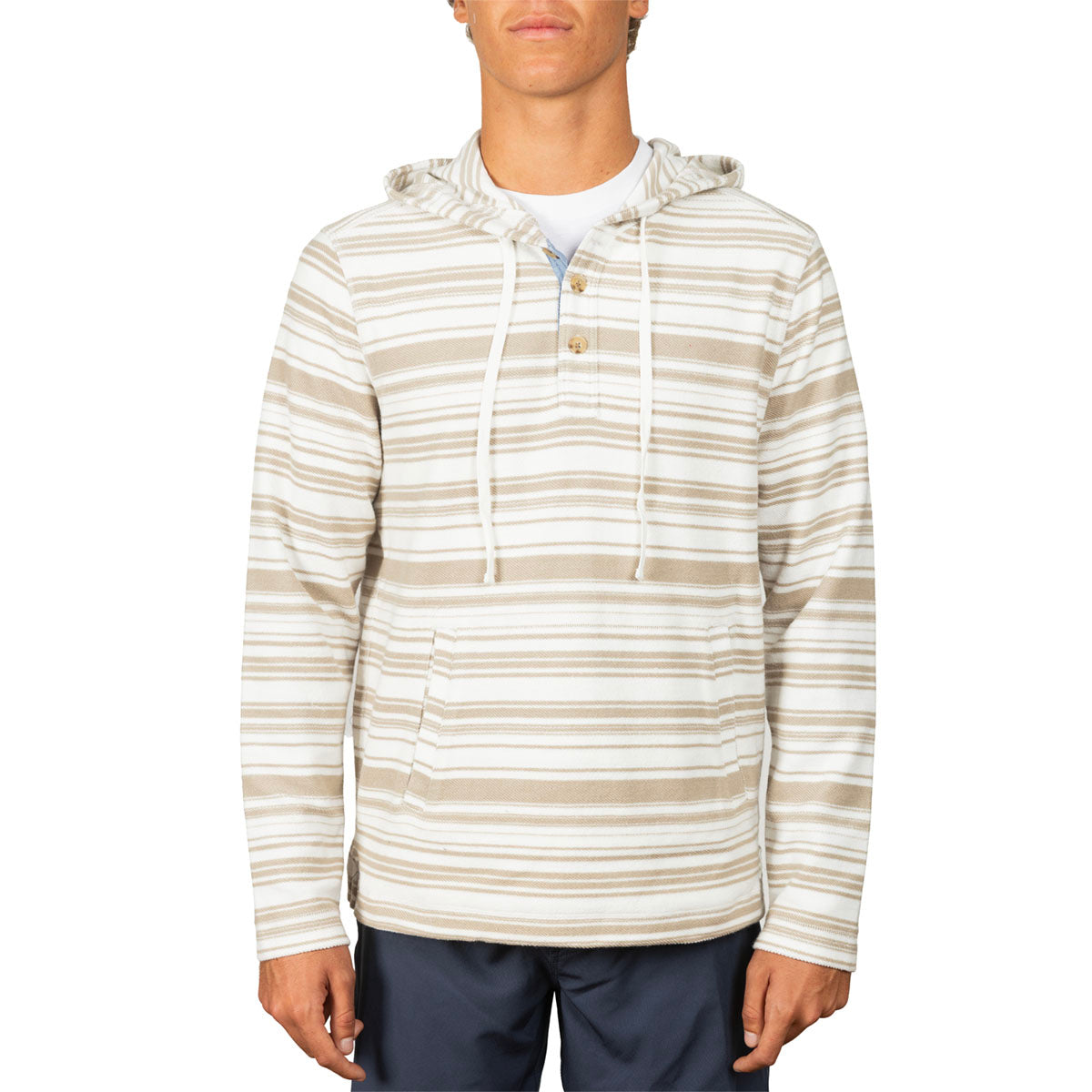 A man wearing a beige and white horizontally striped hooded long-sleeve shirt with a drawstring hood and a small button placket, paired with navy pants, against a plain white background.