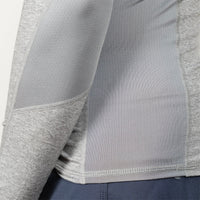 Close-up of a light gray athletic long-sleeve top with textured mesh and heathered fabric panels, shown on a model wearing dark blue bottoms.