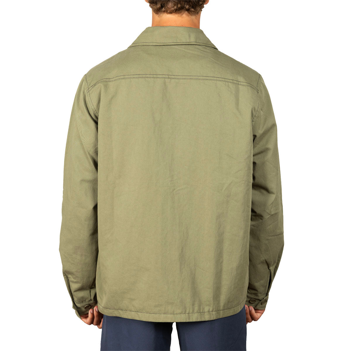 A man viewed from the back wearing an olive green utility jacket and dark blue pants, set against a plain white background.