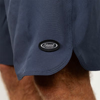 Close-up of navy blue athletic shorts worn by a model, featuring a black oval patch with the 'Stewart' logo on the side hem.