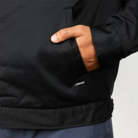 Close-up of a person wearing a black jacket, showing a hand in a side pocket and a small white embroidered Stewart logo near the lower front.