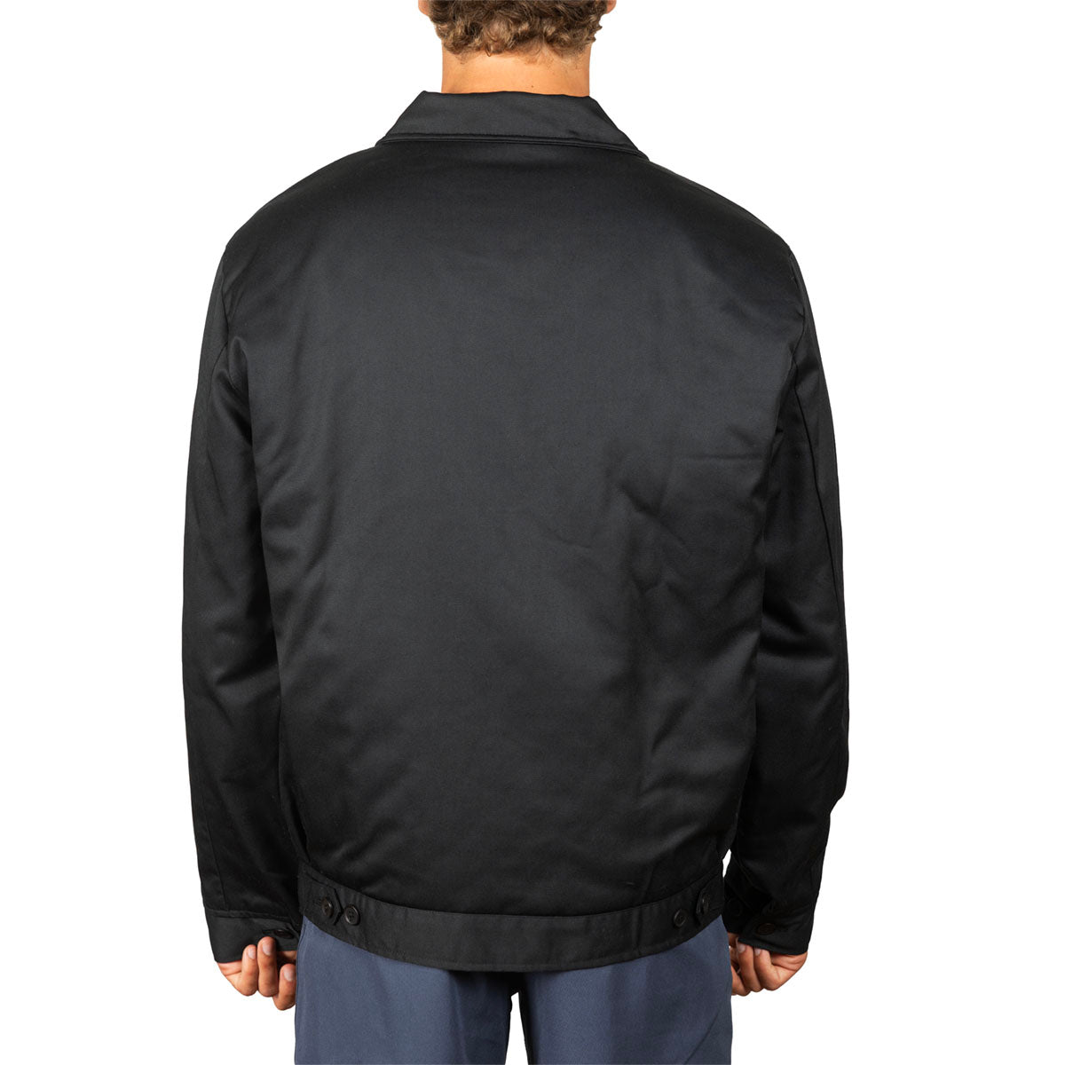 A man viewed from the back wearing a black jacket and blue pants against a plain white background.