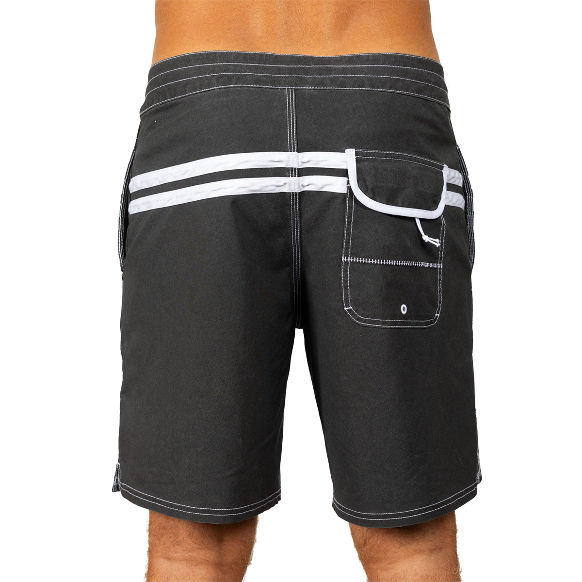 Rear view of a person wearing dark charcoal board shorts with white contrast stitching, a side pocket, and two horizontal white stripes across the back waistband, against a plain white background.