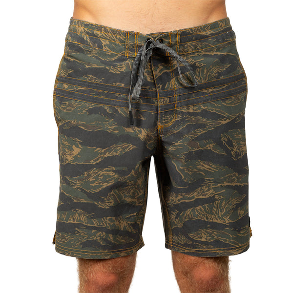 Men's board shorts with an all-over tiger stripe camouflage pattern in olive green, black, and tan, featuring a dark drawstring waist.