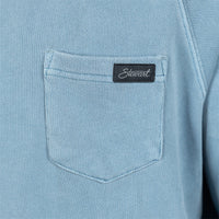 Close-up of a light blue textured fabric garment featuring a front chest pocket with a black rectangular Stewart brand tab.