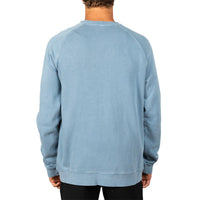 A man viewed from the back wearing a light blue washed crewneck sweatshirt, paired with black pants, against a plain white background.
