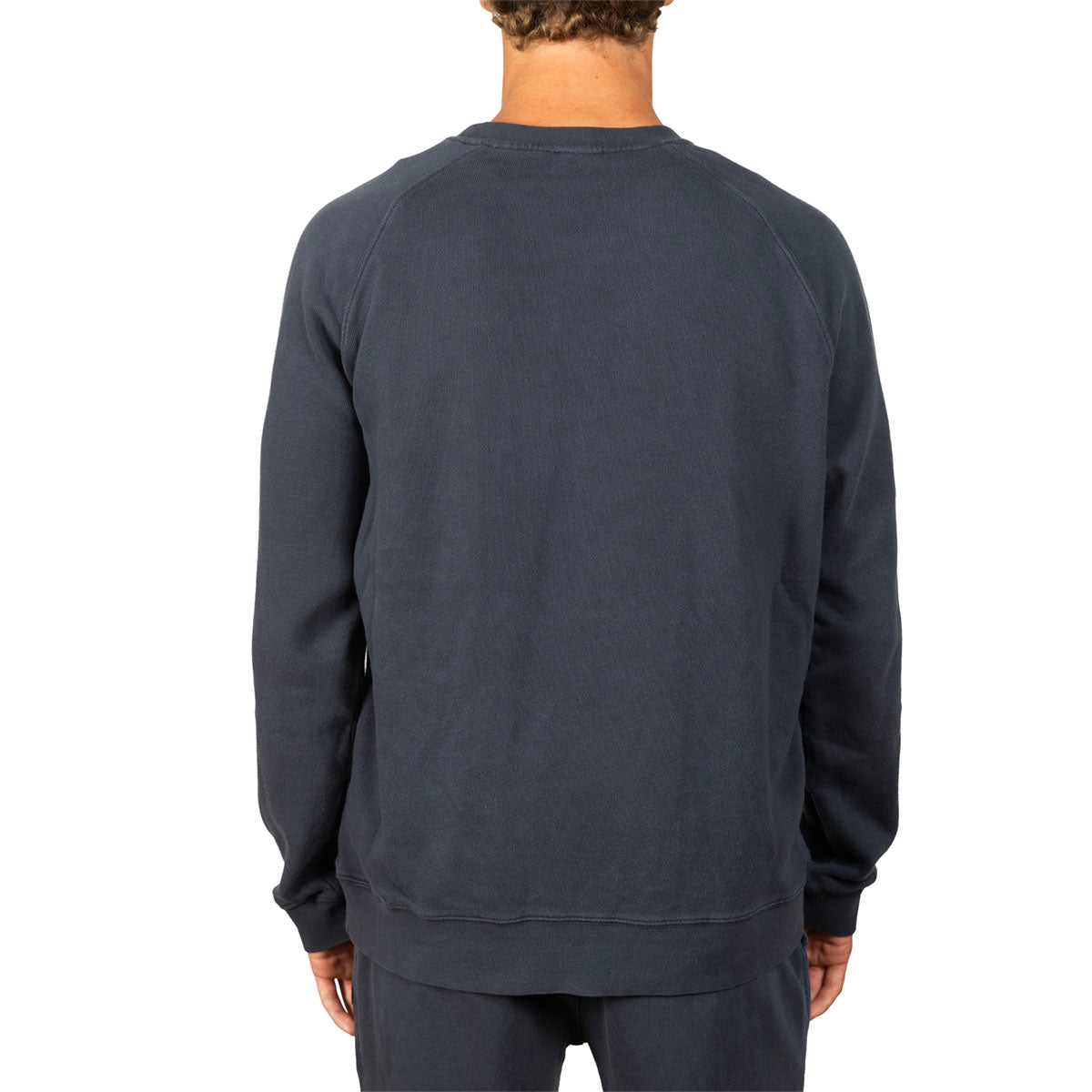 A man viewed from the back wearing a dark slate blue crewneck sweatshirt and matching sweatpants against a plain white background.
