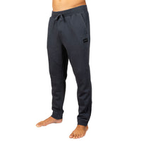 Dark gray sweatpants worn by a model, shown from the waist down on a plain white background. The sweatpants feature an elastic drawstring waist, side pockets, and a small black brand patch on the upper left thigh.