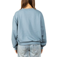 A person shown from the back wearing a dusty blue crewneck sweatshirt and light-wash jeans against a plain white background.