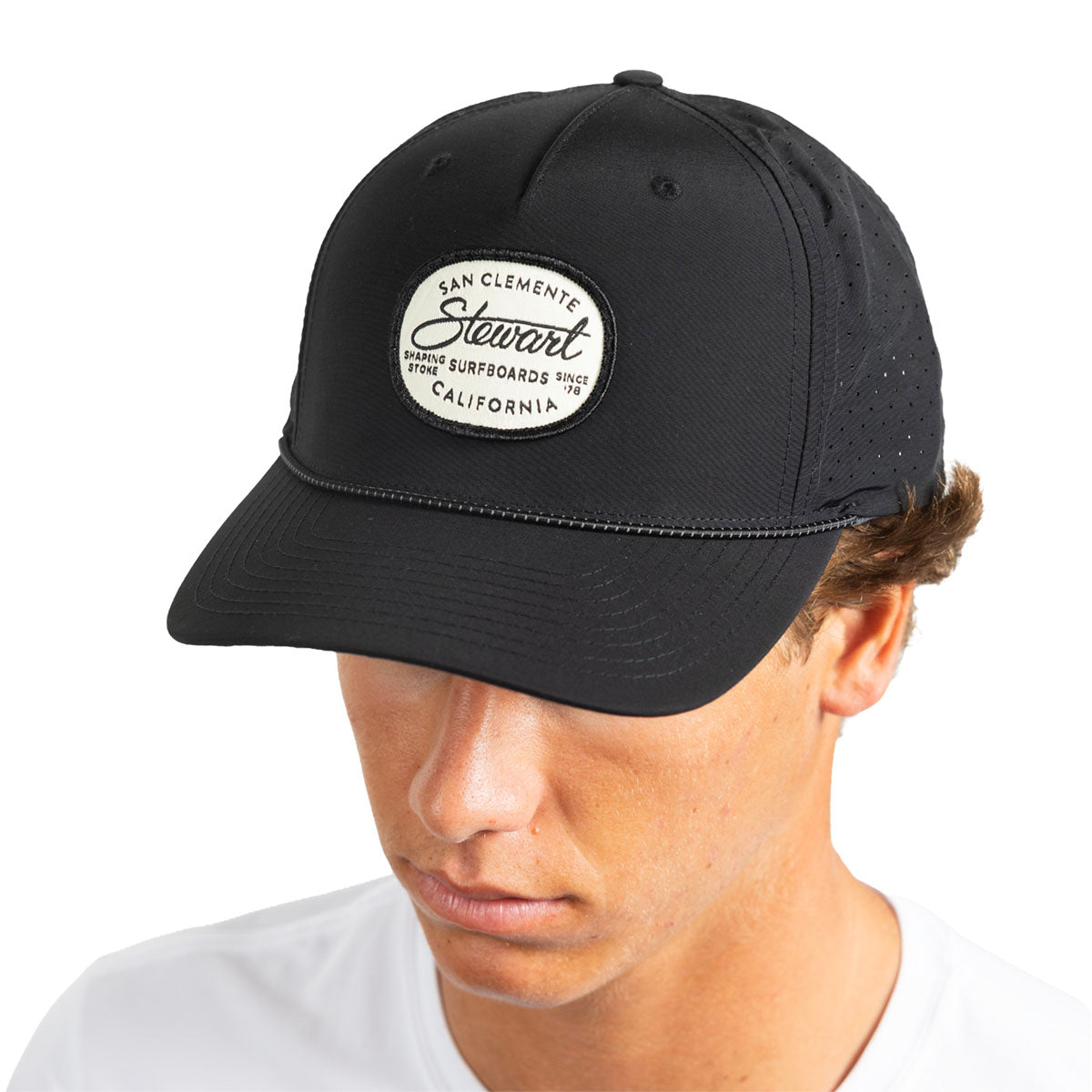 A man wearing a black baseball cap with a white oval patch that reads 'San Clemente Stewart Surfboards California.' The photo is cropped from the chest up against a plain white background.