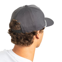 Rear three-quarter view of a man with curly brown hair wearing a dark gray baseball cap with a snapback closure and a white t-shirt, against a solid white background.