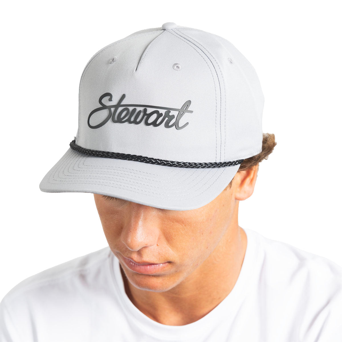 A man wearing a light gray snapback cap with the name 'Stewart' embroidered in black script on the front, above a black braided band, photographed against a plain white background.