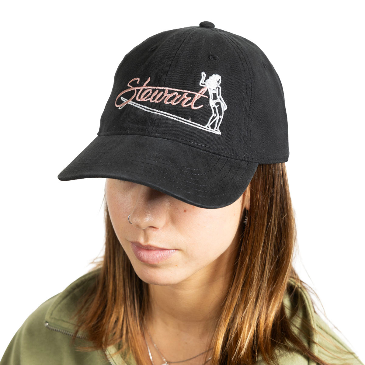 A woman wearing a black baseball cap with 'Stewart' embroidered in white script and a white line-art figure on the front, photographed against a plain white background.