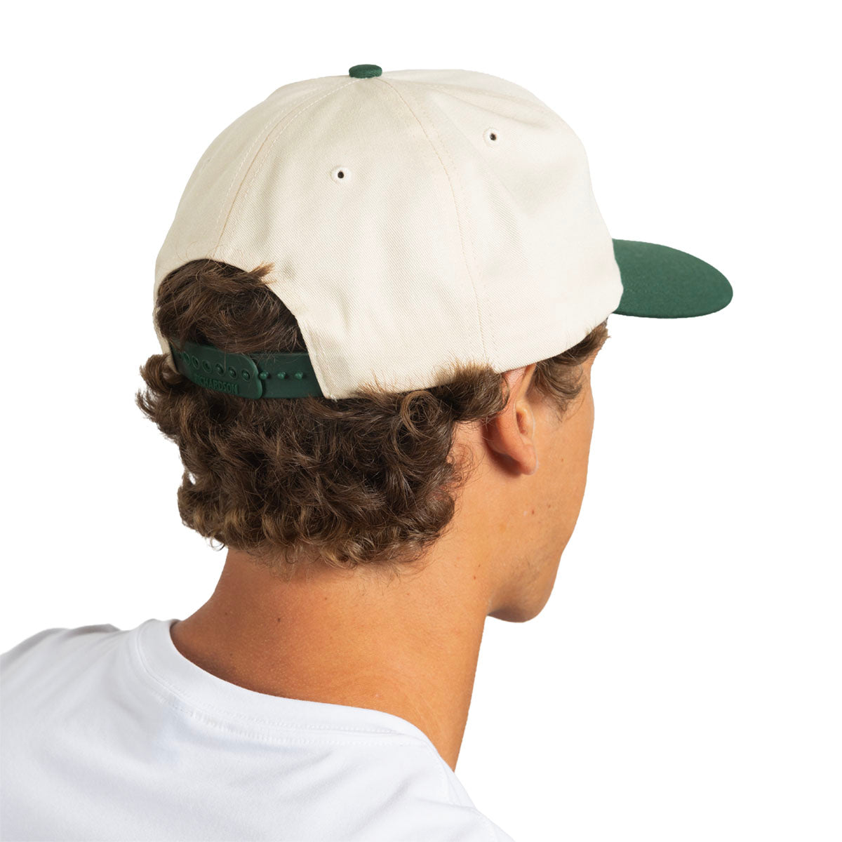 A man shown from the back wearing a cream-colored baseball cap with a dark green visor and matching green back strap, against a plain white background.