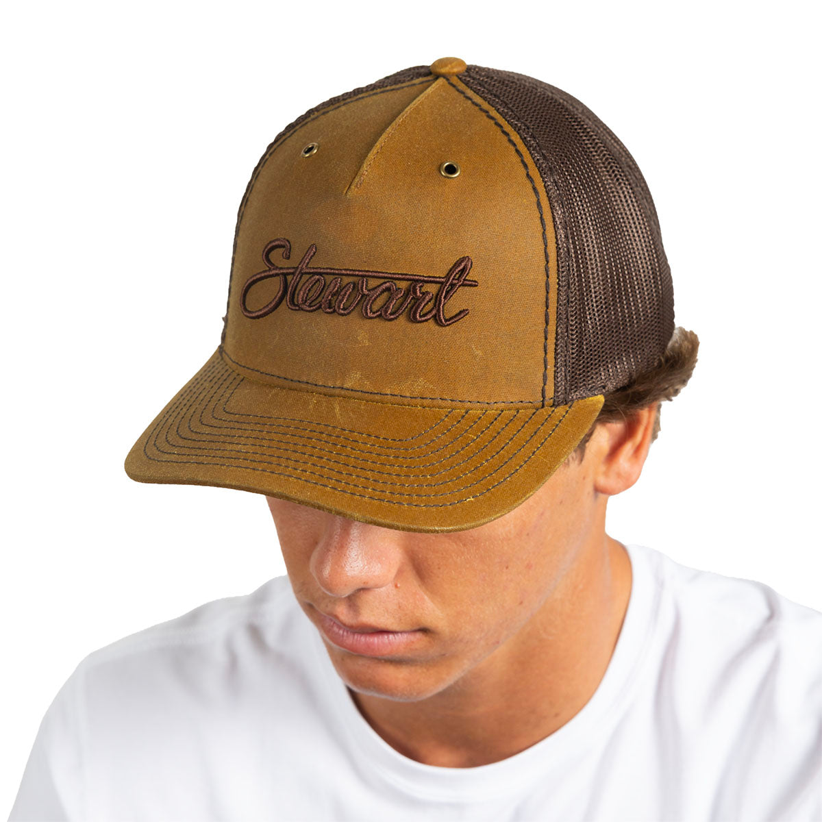 A man wearing a brown and dark brown trucker hat with 'Stewart' embroidered on the front, photographed against a solid white background.