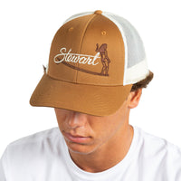 A man wearing a brown and white trucker hat with 'Stewart' and a surfer graphic embroidered on the front, photographed against a plain white background.