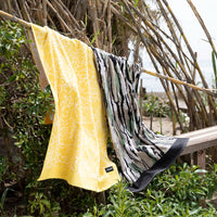 Stewart Yellow Sunshine Towel and Stewart Camo Towel draped over bamboo at the beach