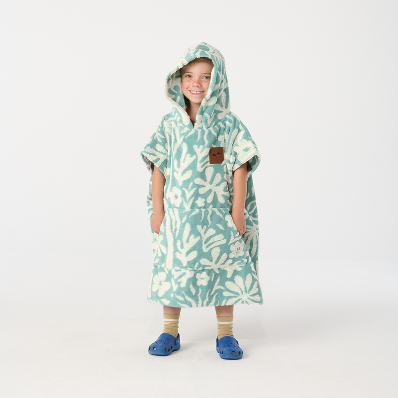 Child wearing a teal and white patterned poncho on a white background