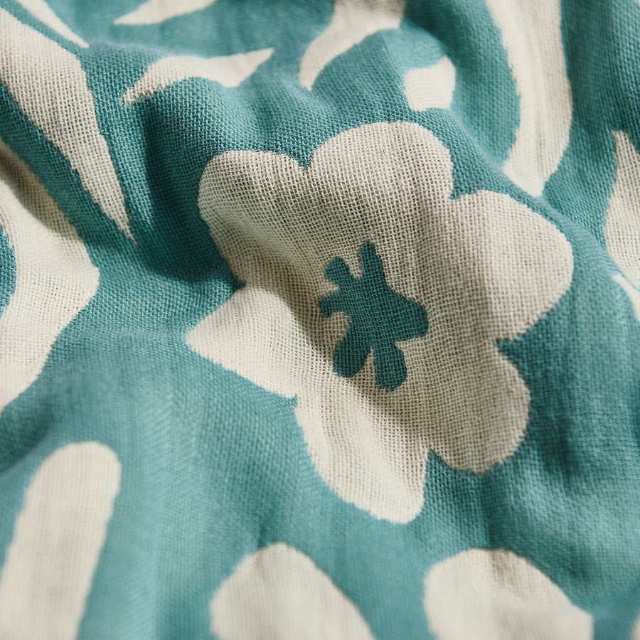 Close-up of a teal and white floral patterned fabric with a green flower emblem.