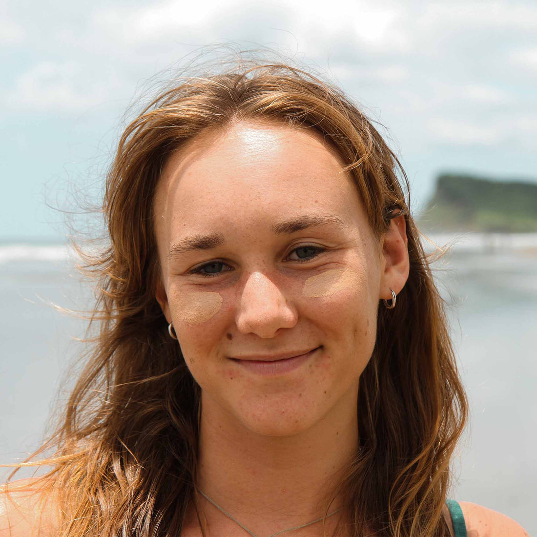 Woman with long brown hair smiling outdoors with a blurred background