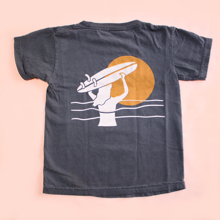 Black t-shirt with a graphic of a hand holding a surfboard against an orange sun on a peach background