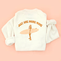 White sweatshirt with 'Just One More Wave' text and a graphic of a surfer on a pink background