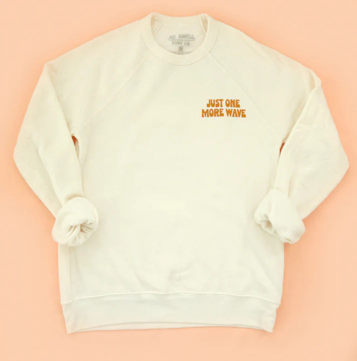 White sweatshirt with 'Just One More Wave' text on a peach background