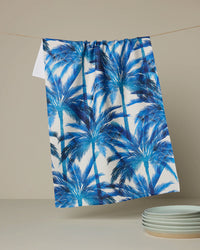 Blue palm tree patterned towel hanging on a line with a neutral background