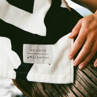 Close-up of a black and white striped garment with 'XO COCO' label, held by a hand on a wooden surface.