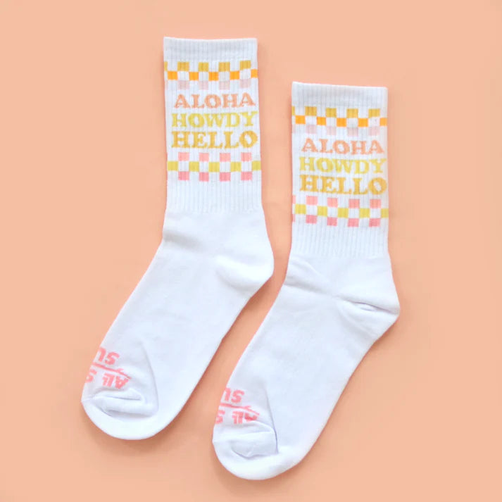 White socks with 'Aloha Howdy Hello' text on a peach background