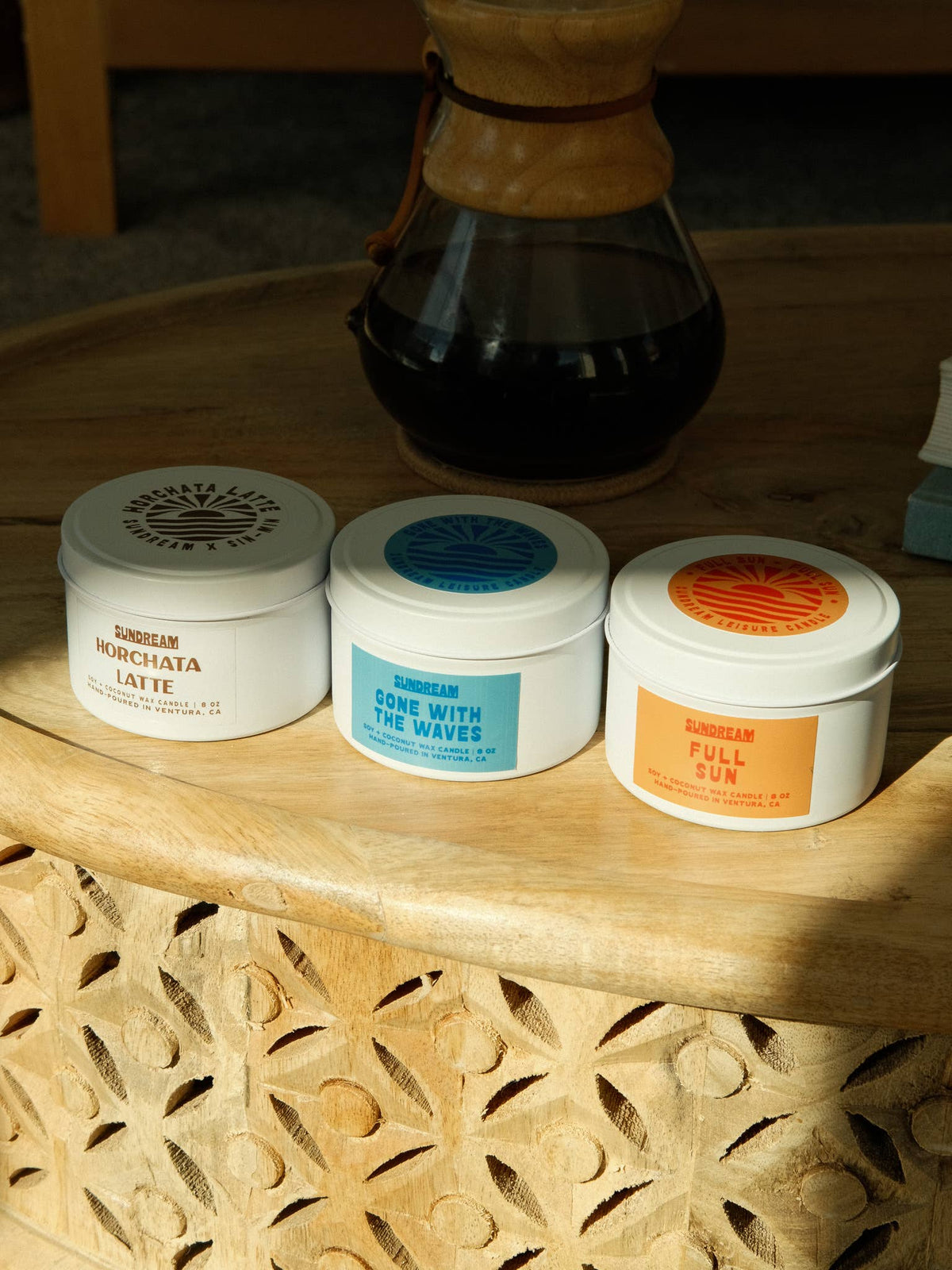 Three containers of different flavors on a wooden surface with a glass of dark liquid in the background.