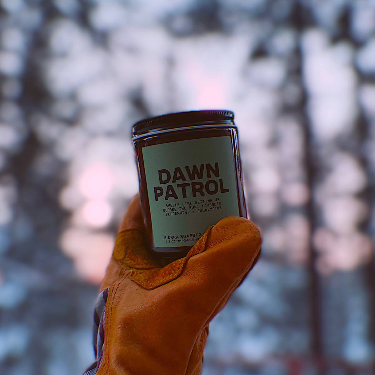 Candle labeled 'Dawn Patrol' held in a gloved hand with a snowy background