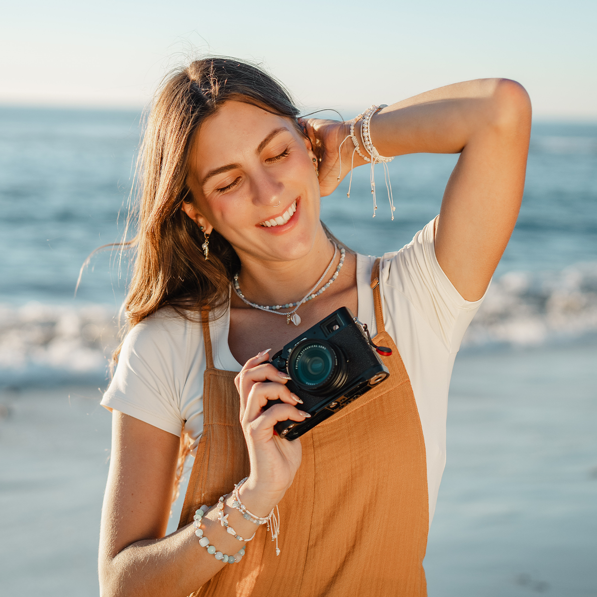 Woman holding a camera on a beach with ocean in the background